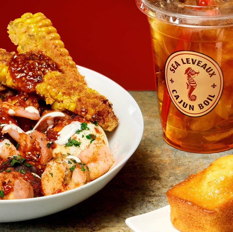 Cajun shrimp boil with corn, potatoes, and sauce, next to a Sea Leveaux iced tea.