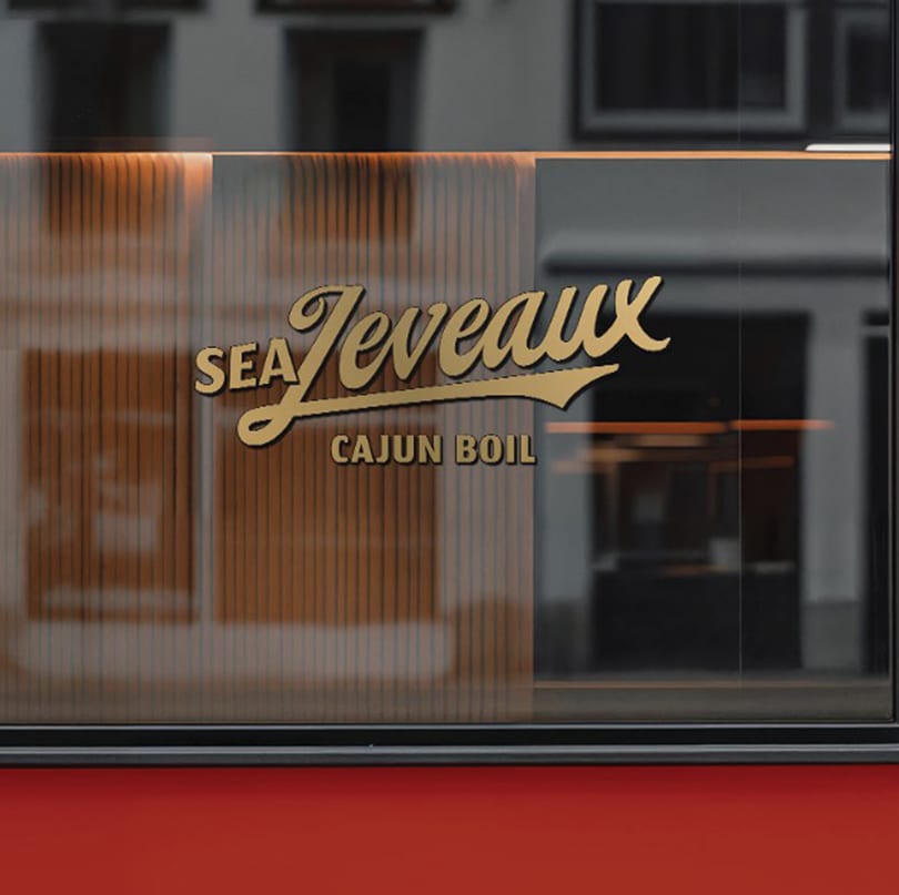 Gold "Sea Jeveaux Cajun Boil" logo on a dark glass window with a red bottom.