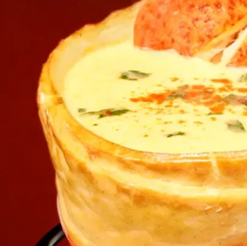 Creamy soup in a bread bowl, garnished with herbs and red pepper flakes.
